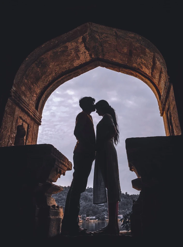 3) Romantic silhouette of a couple having a moment under an old arched building at sunset.
